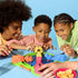 Hasbro Hungry Hungry Hippos family play moment with smiling kids leaning over the colorful green and blue board, pressing levers to help their hippos snap marbles in energetic competition.