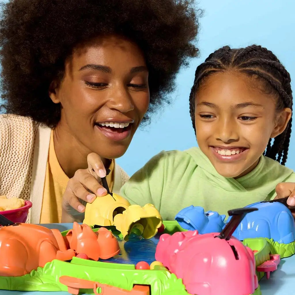 Hasbro Hungry Hungry Hippos scene featuring a joyful adult and child engaging with yellow and blue hippos as red marbles roll across the shiny blue surface in a fun tabletop game session.
