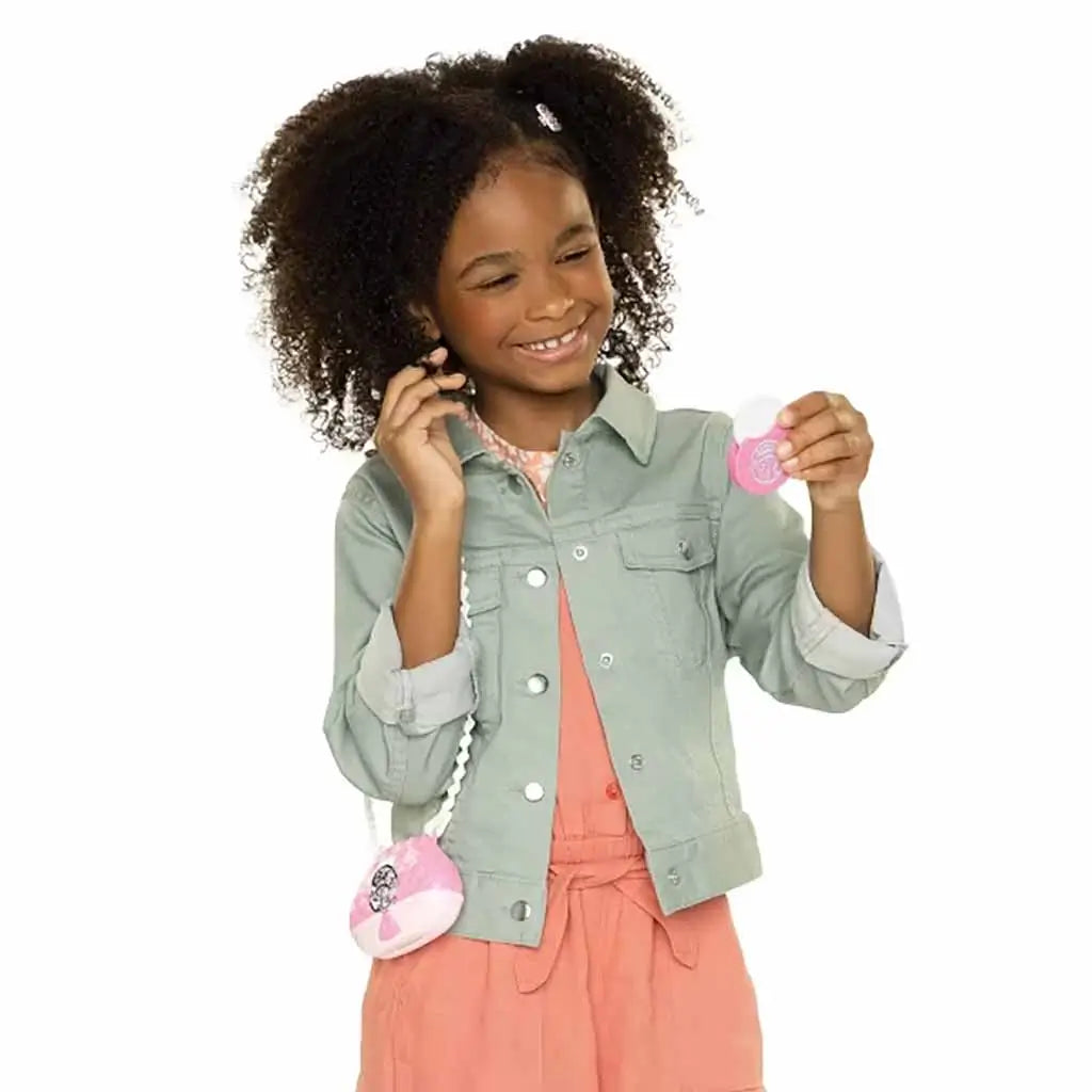 Smiling child holding Disney Princess Style Chic Petites toy purse and accessories, wearing a mint green jacket and coral dress, enjoying pretend play fun.