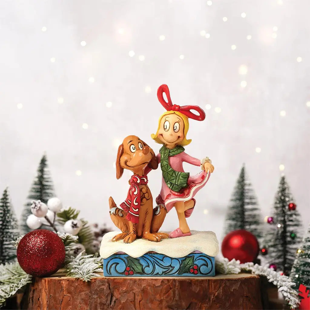 Jim Shore figurine of Cindy Lou Who and Max displayed in a holiday scene with snow, trees, and ornaments, standing on a festive log base.