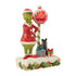 Angled close-up of Jim Shore Grinch figurine showing raised hand beside light-up stop sign with decorative gifts and holiday snow textures.