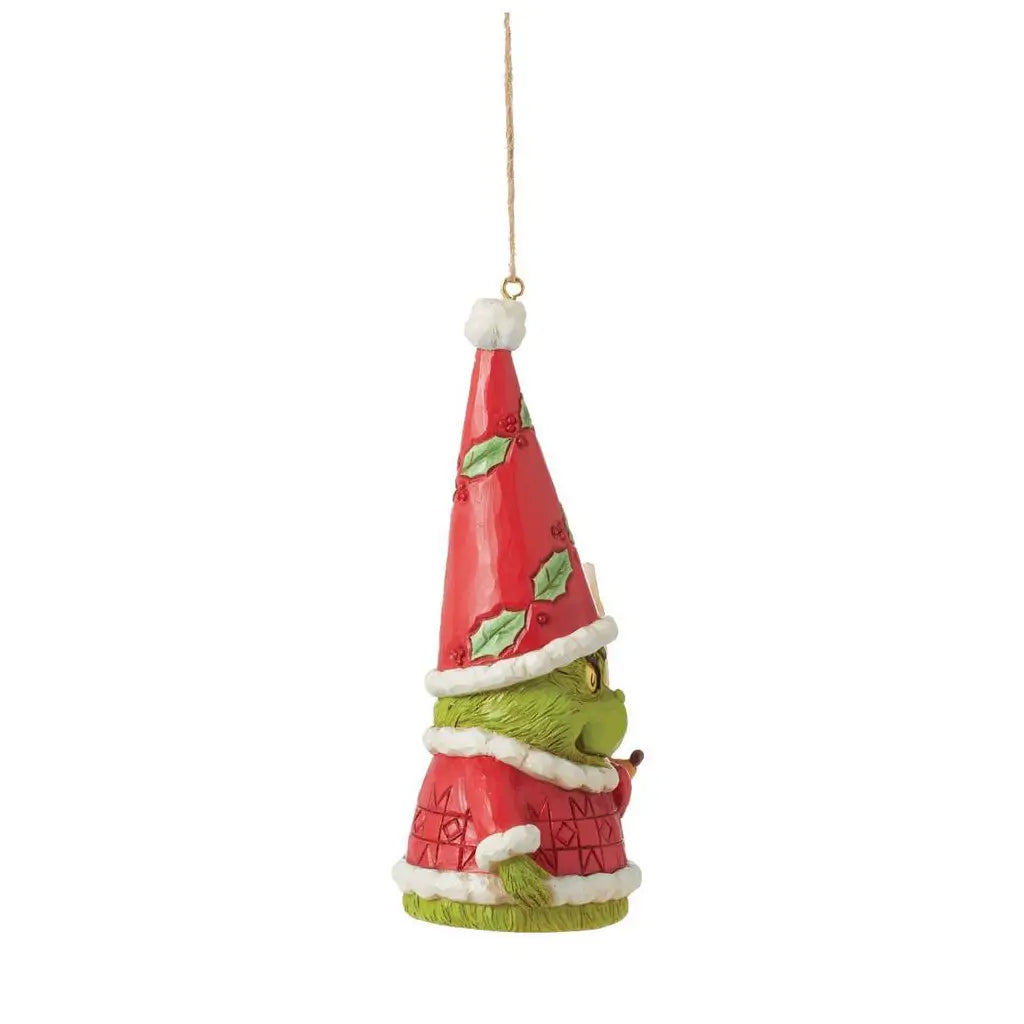 Side view of Jim Shore Grinch gnome ornament with tall red hat and green mittens, showing detailed textures and holding a red heart, standing beside Max.