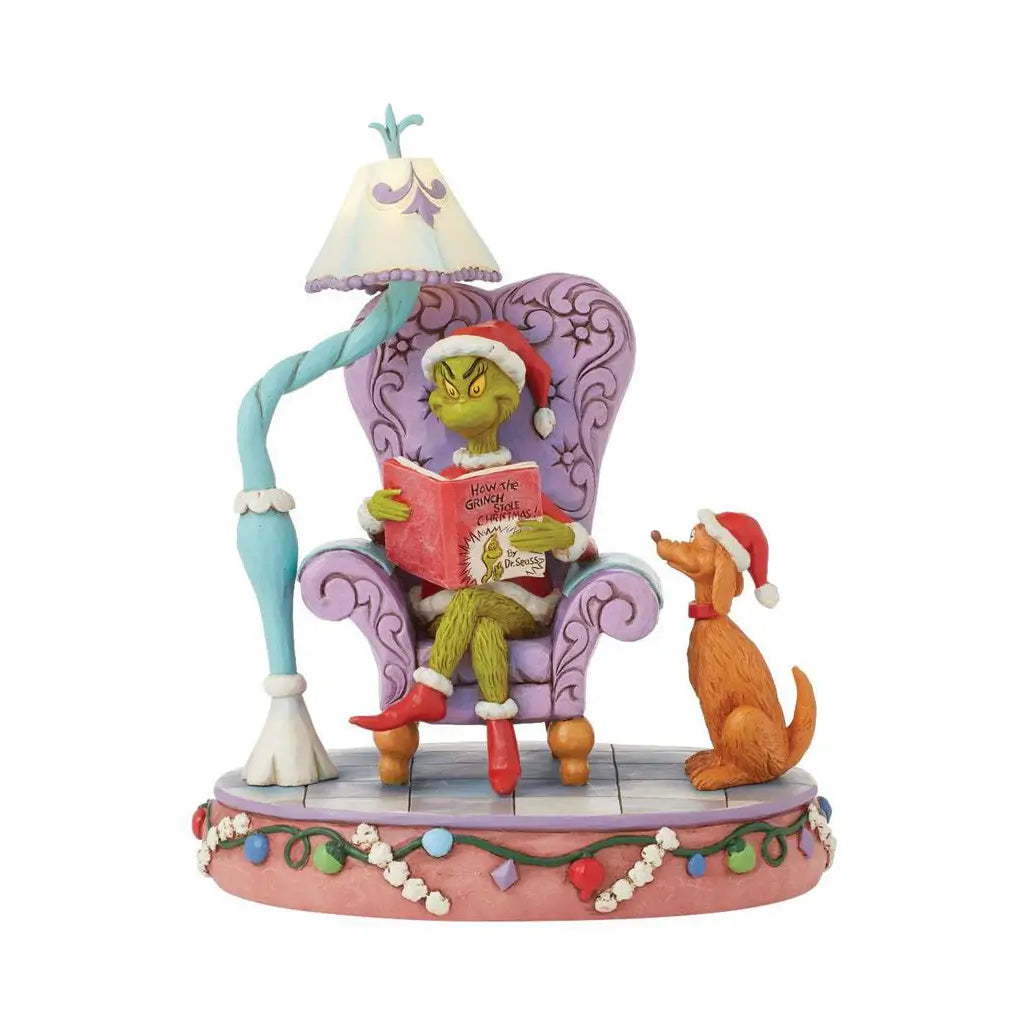 Frontal view of Jim Shore Grinch LED figurine depicting the Grinch reading in a purple chair next to Max, lit by a lamp, with detailed Christmas-themed base.