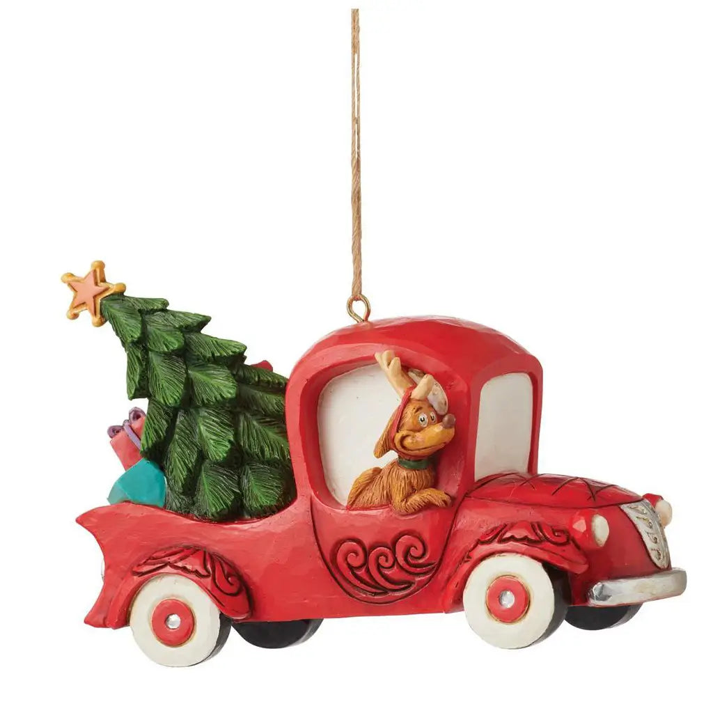 Side angle of Jim Shore ornament showing Max at the wheel of a red truck, transporting a large green Christmas tree and stacked gifts.
