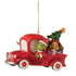 Full side view of Jim Shore ornament with Grinch driving a red Christmas truck, Cindy Lou Who sitting beside gifts and a tree in the back.