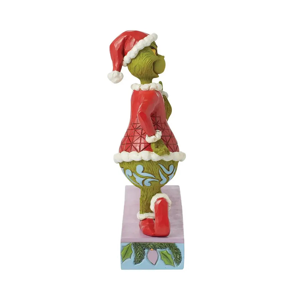 Alternate side view of Jim Shore "Merry Grinchmas" figurine with the Grinch in red and green outfit posed beside decorated holiday text display.