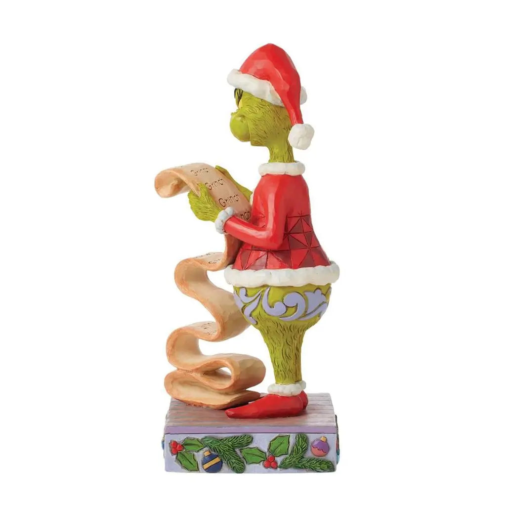 Alternate side view of Jim Shore Grinch figurine in Santa attire, reading a curled name list, on a purple holiday base with evergreen and ornament accents.