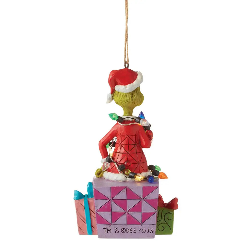 Rear view of Jim Shore Grinch ornament with the Grinch seated on a wrapped gift, wearing holiday lights and a Santa hat, surrounded by other presents.