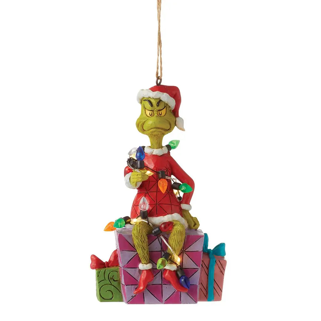 Front view of Jim Shore Grinch ornament with the Grinch frowning while wrapped in multicolored string lights, sitting atop festive presents.