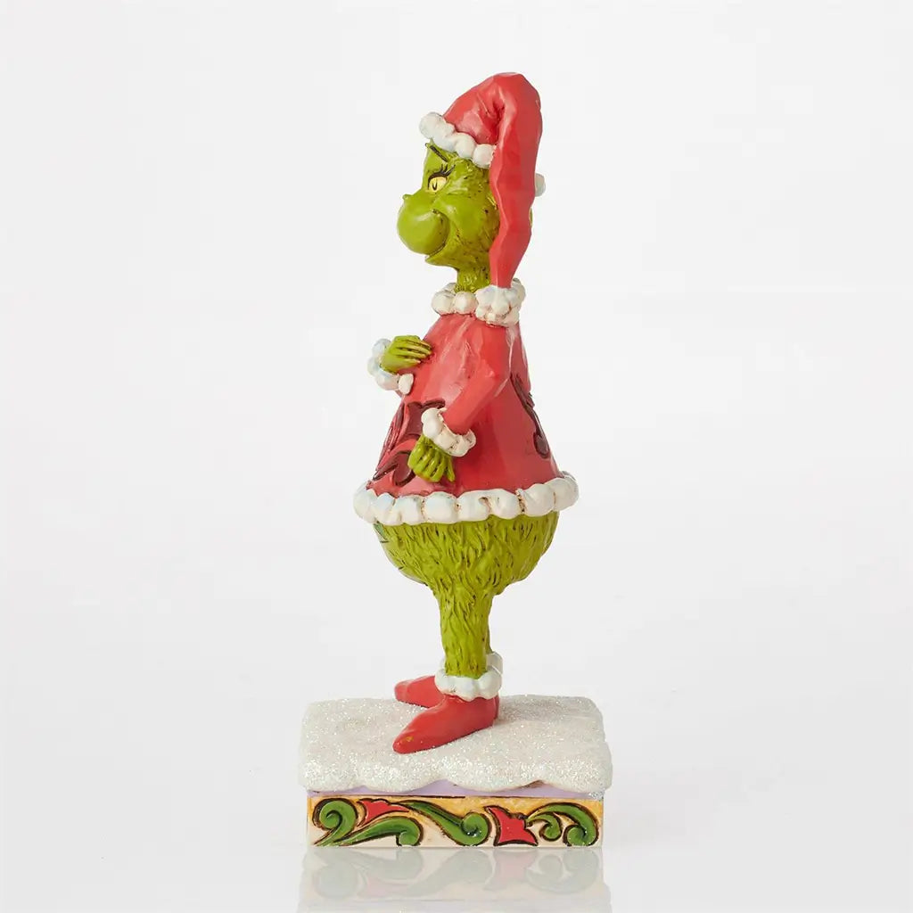 Side view of Jim Shore Grinch figurine showing hand on belly, red Santa outfit with white trim, and patterned green legs, standing on a snowy base.