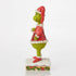 Side view of Jim Shore Grinch figurine showing hand on belly, red Santa outfit with white trim, and patterned green legs, standing on a snowy base.