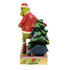 Angled side view of Jim Shore Grinch figurine in red Santa coat, clutching green Christmas tree with gold star, on holly and vine patterned base.