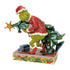 Front angled view of Jim Shore Grinch figurine in red Santa coat, mischievously carrying ornamented tree with presents at feet, on festive holly-trimmed base.