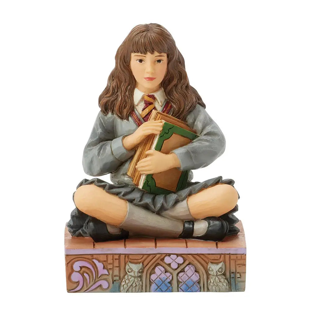 Front view of Hermione Granger Jim Shore collectible figurine, hand-painted with detailed Gryffindor tie, cross-legged pose, decorative base with owls and stained glass motifs.