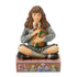 Front view of Hermione Granger Jim Shore collectible figurine, hand-painted with detailed Gryffindor tie, cross-legged pose, decorative base with owls and stained glass motifs.
