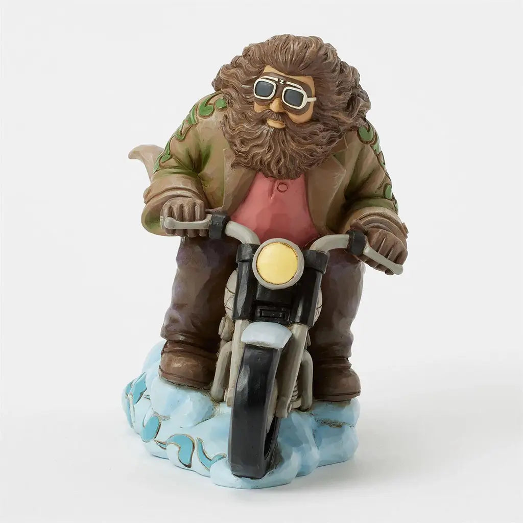 Front view of Jim Shore figurine depicts Hagrid flying enchanted motorbike, brown beard and goggles visible, with headlamp shining above stylized cloud base.