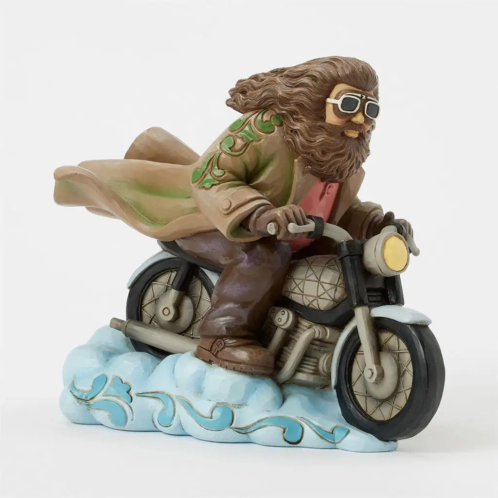 Jim Shore Harry Potter collectible shows Hagrid gripping enchanted motorbike handlebars, wearing goggles and coat, soaring over blue clouds with carved detail.