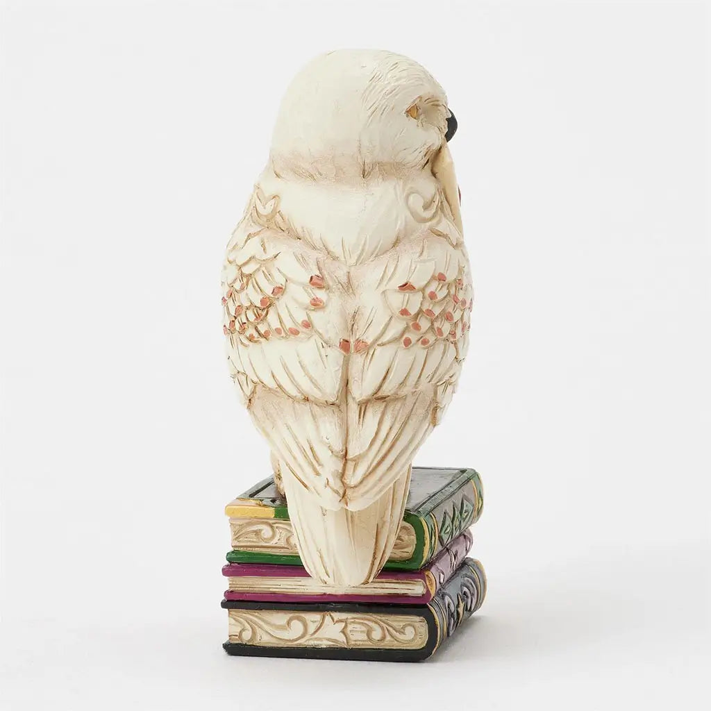 Left side of Jim Shore Hedwig mini figurine shows owl holding Hogwarts letter, intricate feather details, and stacked sculpted books with gilded patterns.