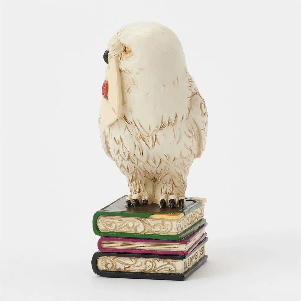 Jim Shore Harry Potter Hedwig mini figurine shows white snowy owl holding Hogwarts acceptance letter, perched on stacked books with ornate carved detail.