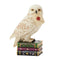 Front view of Jim Shore Hedwig mini figurine depicts owl clutching sealed letter in beak, standing on decorative stack of green, purple, and black books.