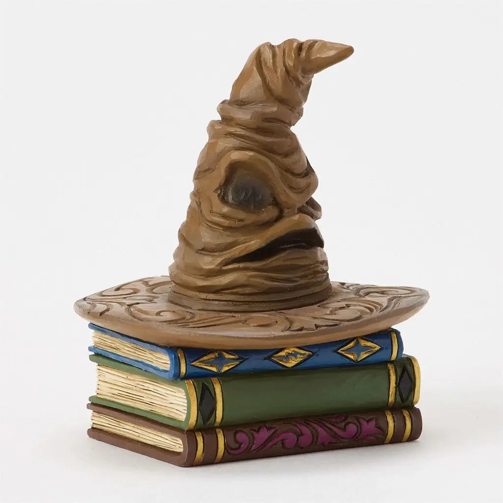 Angled view of Jim Shore Sorting Hat figurine reveals expressive folds and face, placed on sculpted books with gold accents and carved magical motifs.