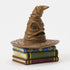 Angled view of Jim Shore Sorting Hat figurine reveals expressive folds and face, placed on sculpted books with gold accents and carved magical motifs.