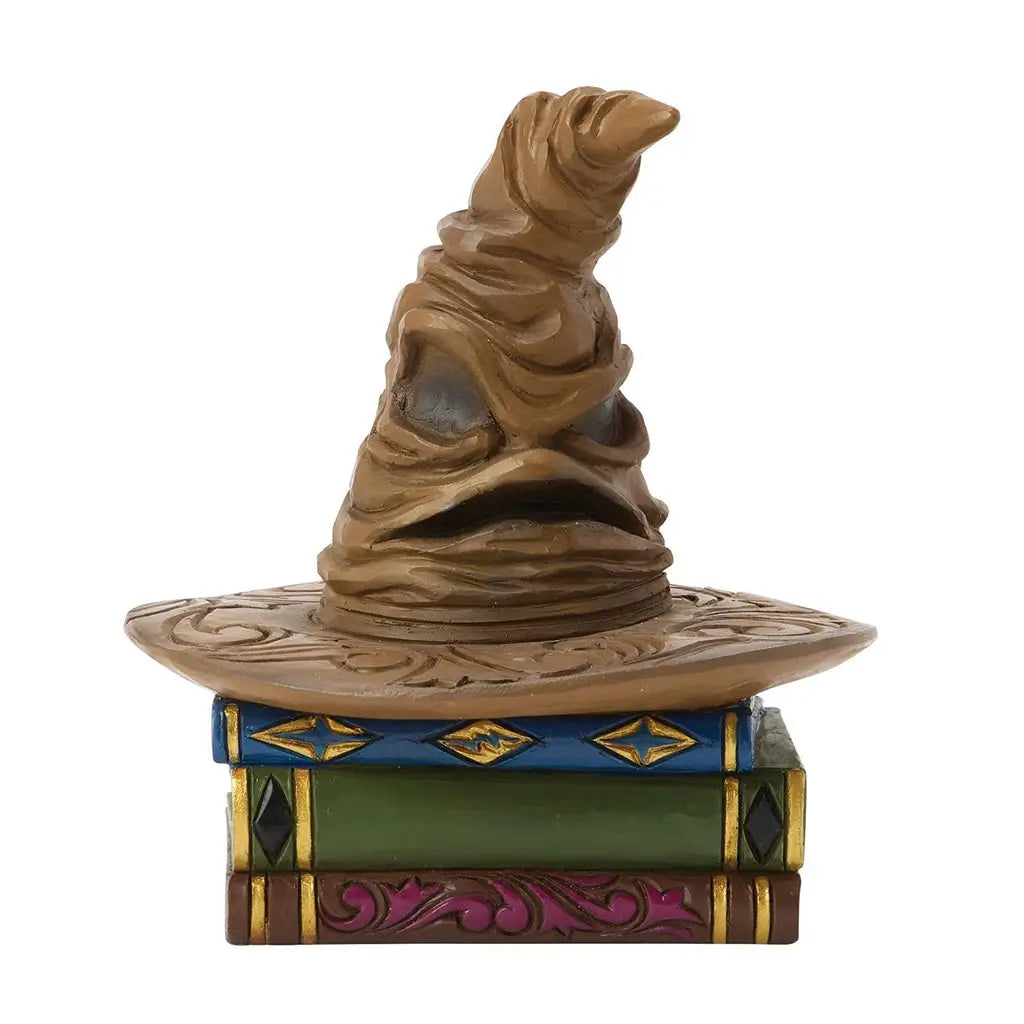 Jim Shore Harry Potter Sorting Hat mini figurine shows wrinkled brown hat with carved details, resting atop colorful stacked books in green, blue, and purple.