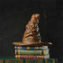 Lifestyle photo of Jim Shore Sorting Hat mini figurine placed on green books, featuring wrinkled brown hat sitting on painted magical book pedestal.
