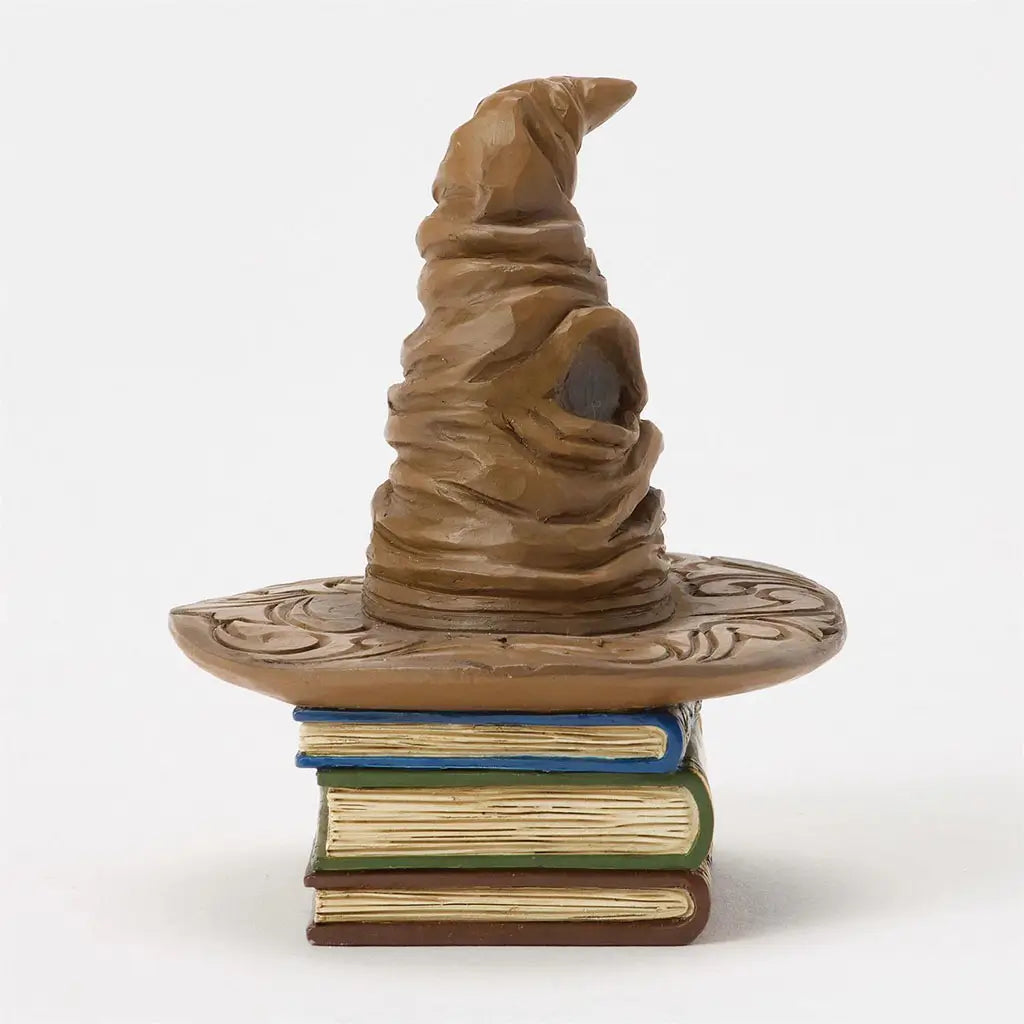 Side view of Jim Shore Sorting Hat mini figurine highlights sculpted creases, tilted tip, and stacked decorative book base with textured spines.