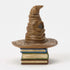 Side view of Jim Shore Sorting Hat mini figurine highlights sculpted creases, tilted tip, and stacked decorative book base with textured spines.