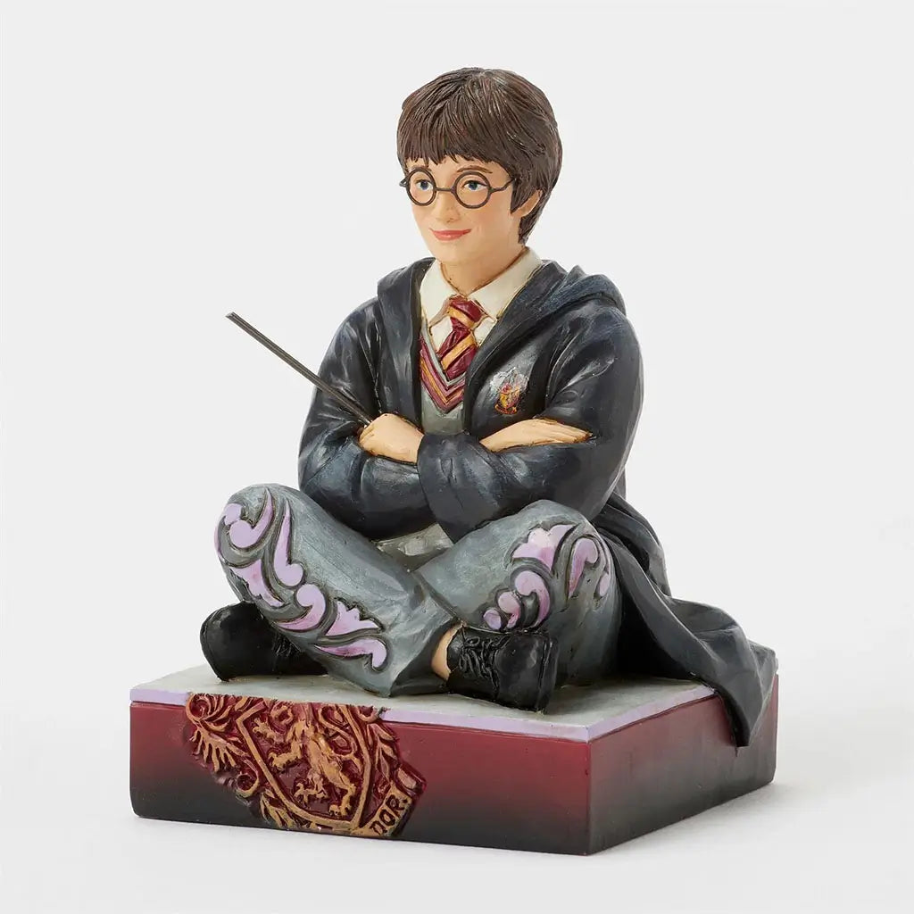 Right angled view of Jim Shore Harry Potter figurine, showing sculpted black robe folds, wand, and Gryffindor crest on decorative maroon base.