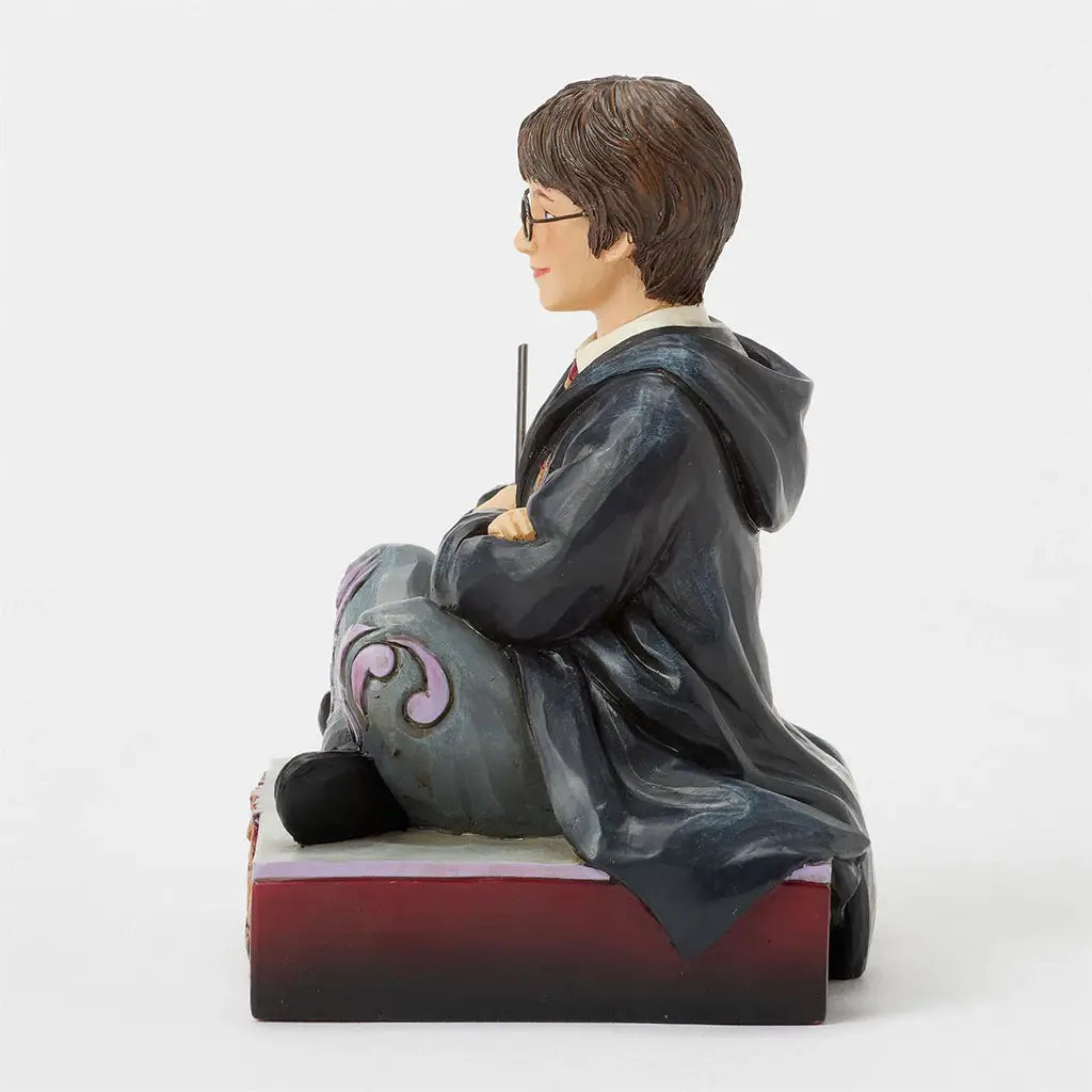 Right side view of Jim Shore Harry Potter figurine, highlighting carved robe details, wand in hand, and seated pose atop maroon crest-adorned base.