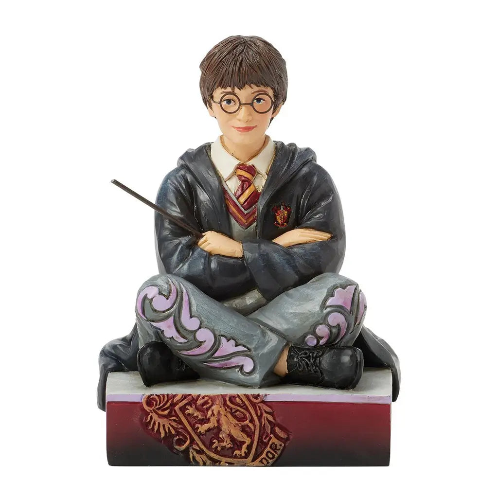 Front view of Jim Shore Harry Potter figurine, hand-painted with glasses, Gryffindor robes, and wand in hand, seated cross-legged on a base with crest details.