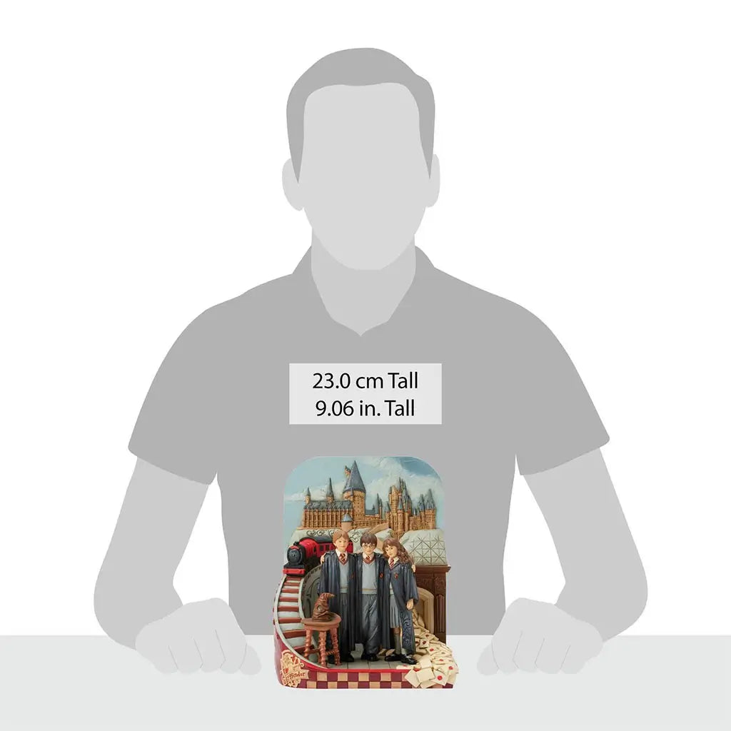 Harry Potter figurine by Jim Shore stands 23 cm tall, showing Harry, Ron, and Hermione in Hogwarts robes with castle backdrop, Sorting Hat, letters, and red train accent.