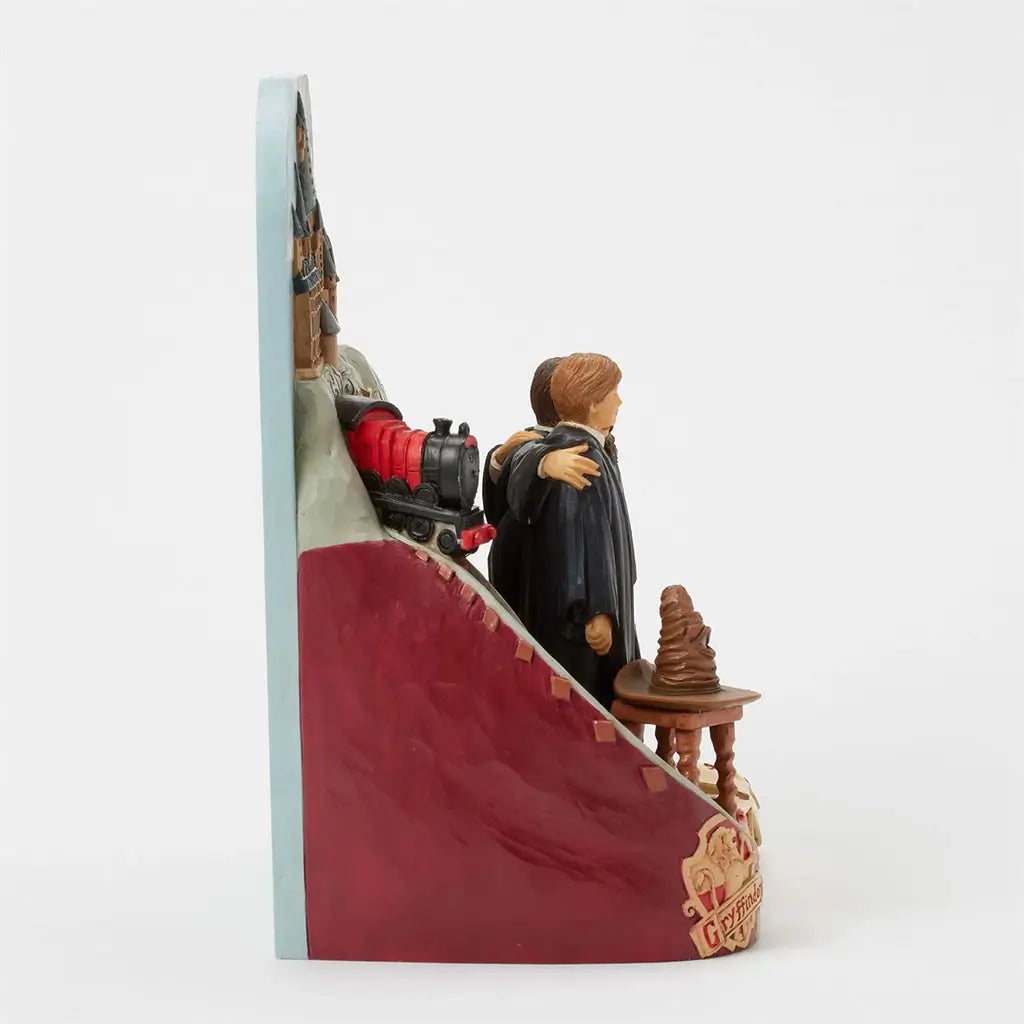 Side view of Jim Shore Harry Potter figurine highlights Gryffindor crest, Hogwarts Express engine, trio in robes, Sorting Hat, and staircase with Hogwarts letters.