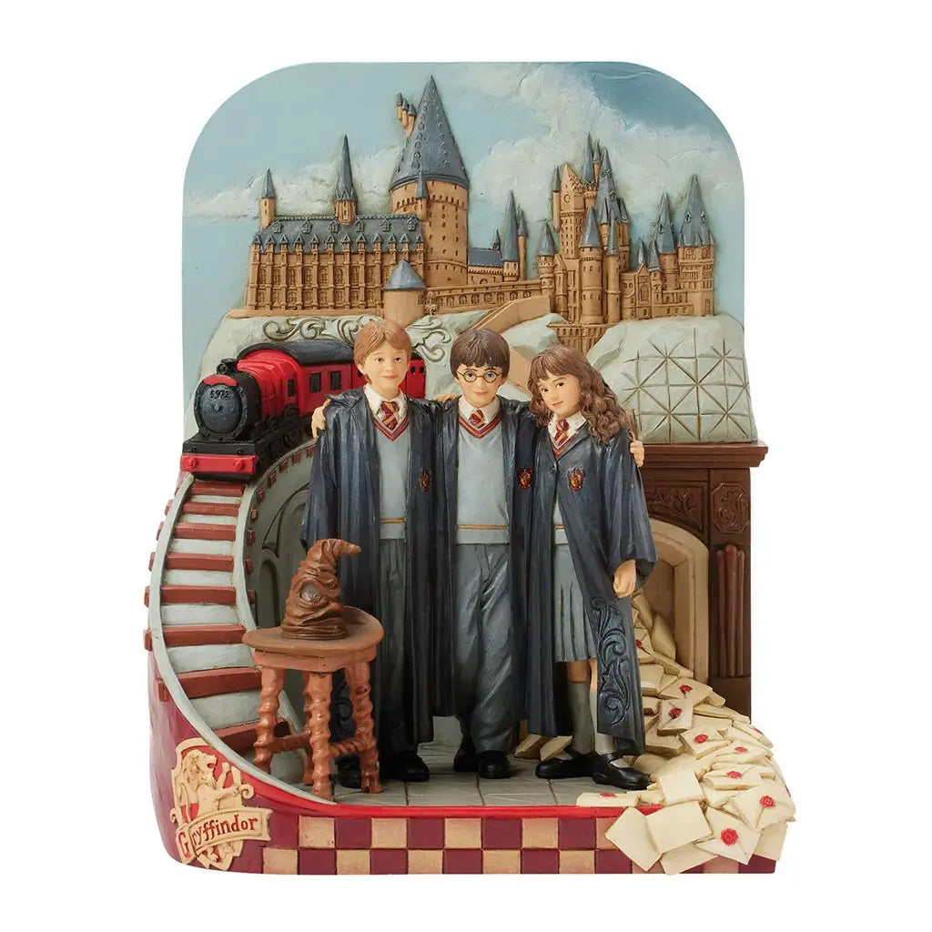 Front view of Jim Shore Harry Potter figurine with Hogwarts castle background, trio in robes, Sorting Hat on wooden stool, red train, and Gryffindor crest detail.