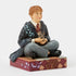 Angled view of Ron Weasley Jim Shore figurine, detailed in red hair, grey pants, black shoes, and maroon tie, holding Scabbers while seated on a decorative platform.