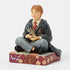 Right angled view of Ron Weasley figurine by Jim Shore, hand-painted in Gryffindor uniform, seated cross-legged holding Scabbers atop a red and gold patterned base.