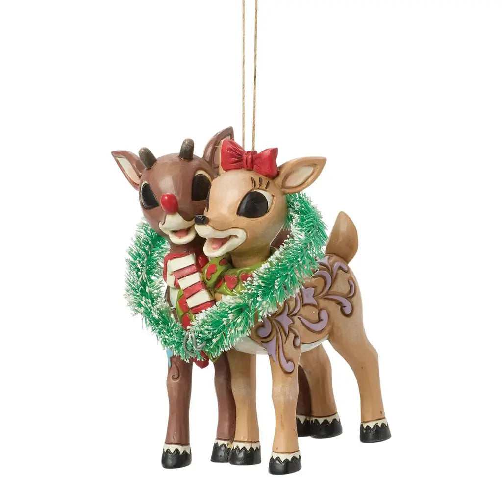 Three-quarter view of Jim Shore Rudolph and Clarice ornament, showing folk art carvings, holiday scarves, and a bright green tinsel wreath.