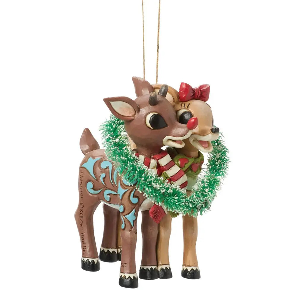 Angled view of Jim Shore Rudolph and Clarice ornament, depicting reindeer couple with red and white scarves entwined in a green tinsel heart wreath.