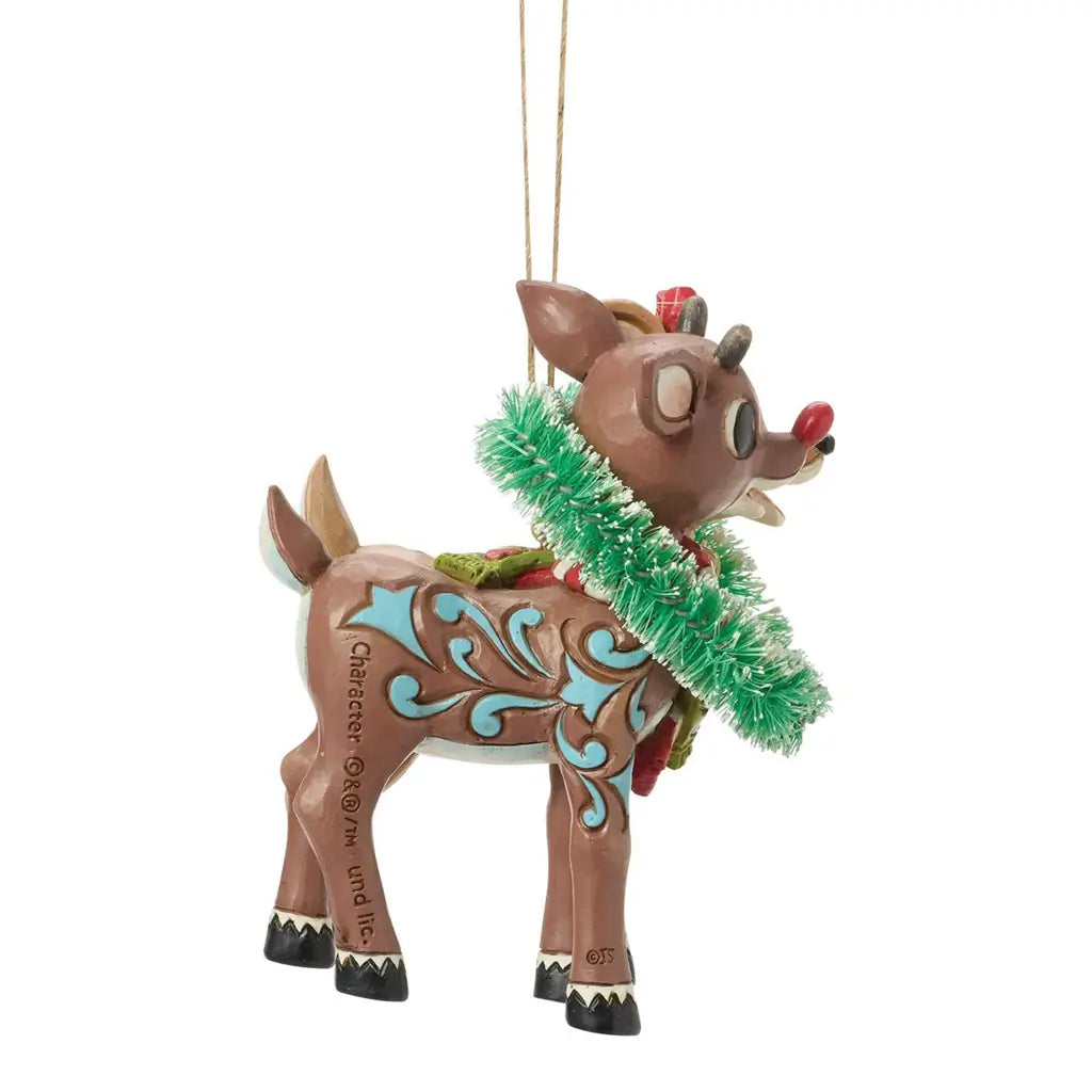 Side view of Jim Shore Rudolph ornament, showing reindeer with red nose and blue swirl patterns wearing a green tinsel heart wreath.