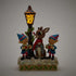 Light-up Jim Shore Rudolph figurine featuring two elves caroling under a glowing lamppost, detailed with holly leaves, snowy texture, and vibrant blue and red painted accents.