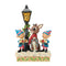 Jim Shore Christmas figurine of Rudolph and elves under a lamppost, hand-carved with folk art patterns, holly garlands, and snowy base, ideal for festive holiday displays.