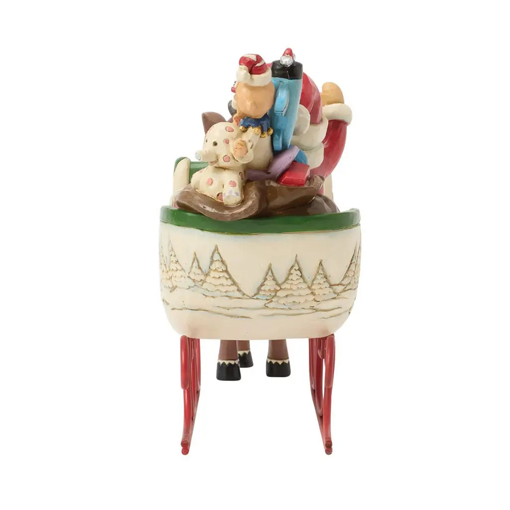 Back view of Jim Shore Rudolph and Santa sleigh figurine, showing engraved snowy trees and toys peeking from the sleigh.
