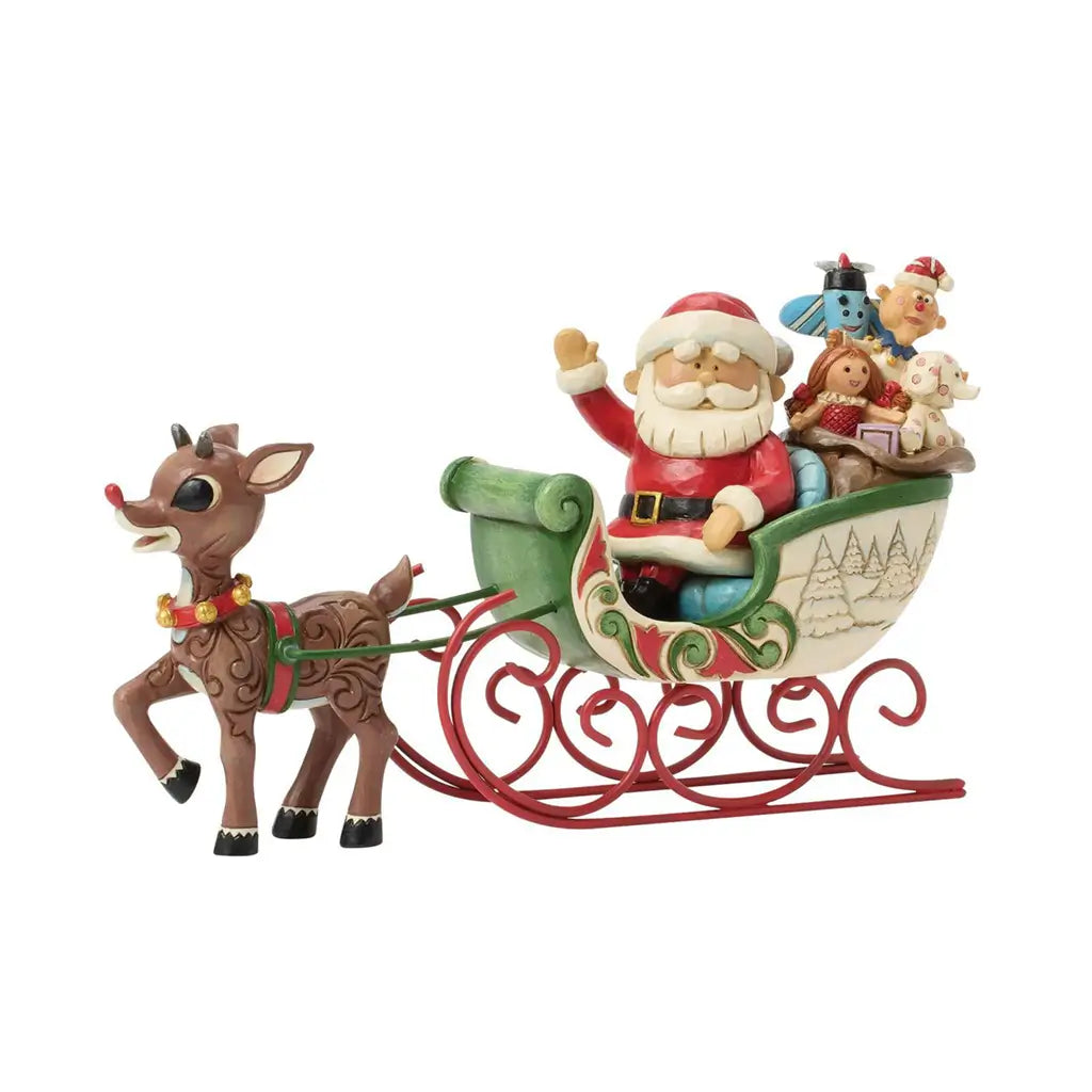 Jim Shore figurine of Rudolph pulling Santa’s sleigh filled with toys, featuring folk art carvings, red runners, and hand-painted holiday details.