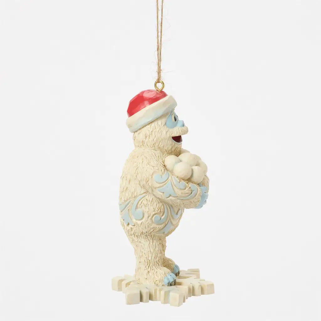 Side view of Jim Shore Bumble Christmas ornament, holding snowballs while wearing a Santa hat, with blue folk art patterns on white fur.