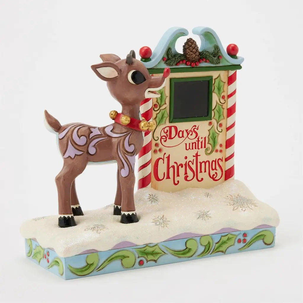 Angled view of Jim Shore Rudolph countdown figurine, showing festive striped calendar frame, red lettering, and folk art detailing on reindeer and base.