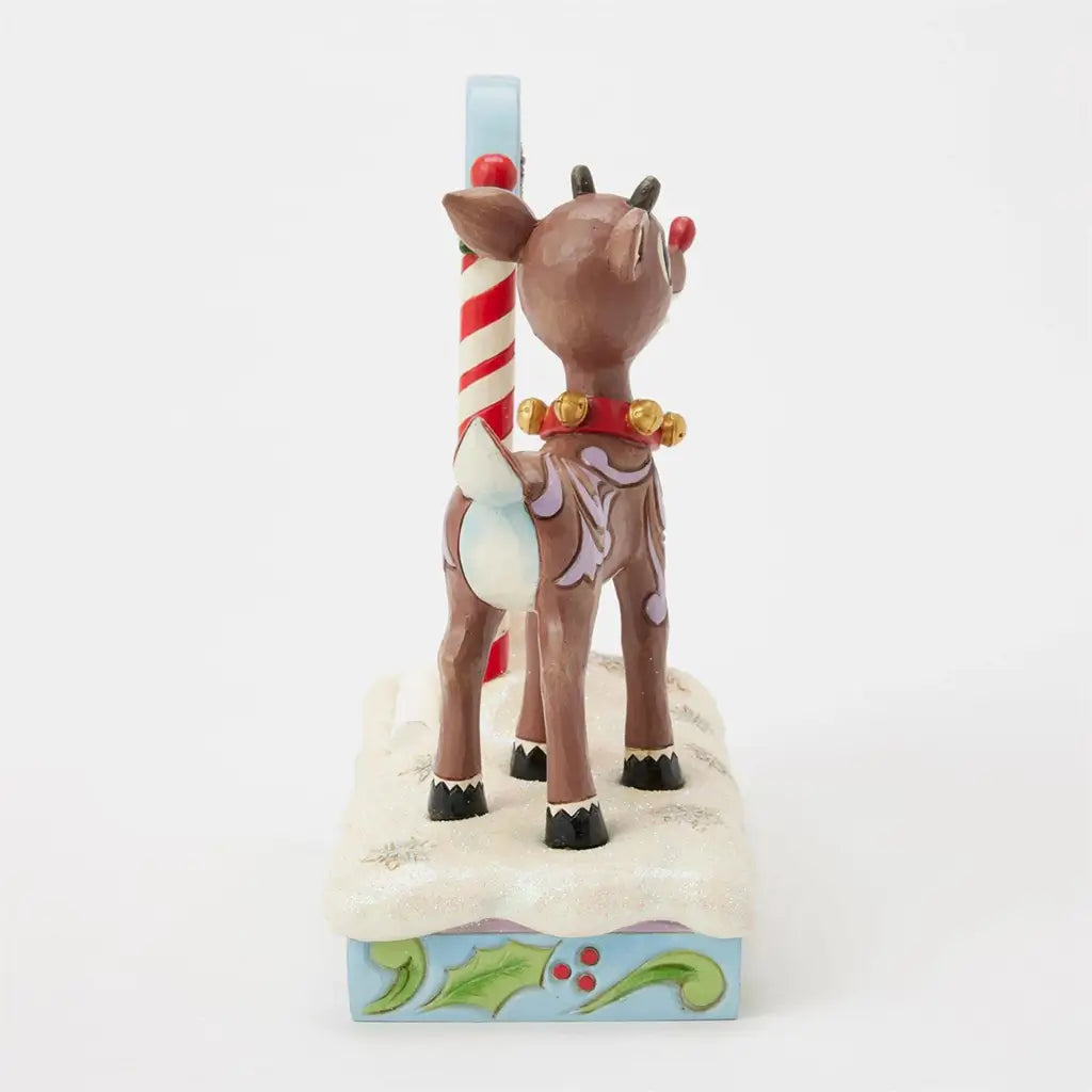 Rear angled view of Jim Shore Rudolph countdown figurine, showing reindeer with gold bell collar and red nose beside striped holiday calendar frame.
