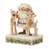 Angled front view of Jim Shore cream Santa figurine holding reindeer, including red-nosed Rudolph, on snowy holly-trimmed base, against plain white background.