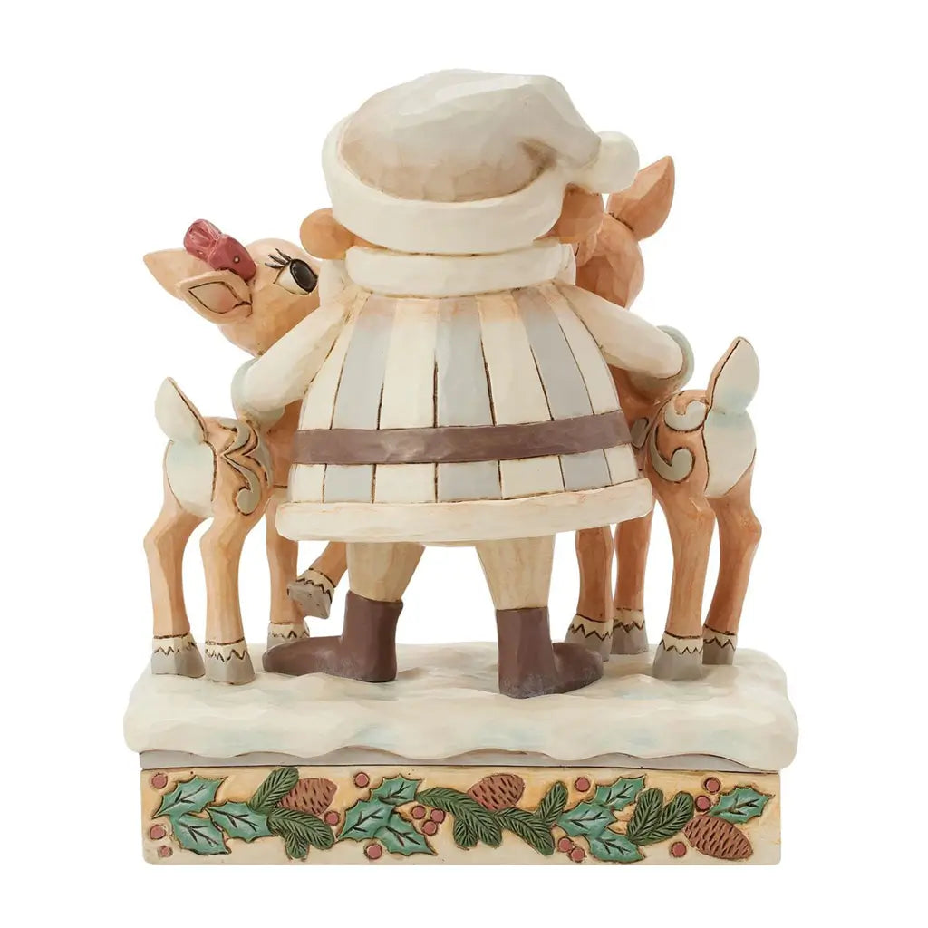 Back view of cream and brown Jim Shore Santa figurine with arms around two reindeer on snowy base, holly and pinecone trim, set against plain white background.